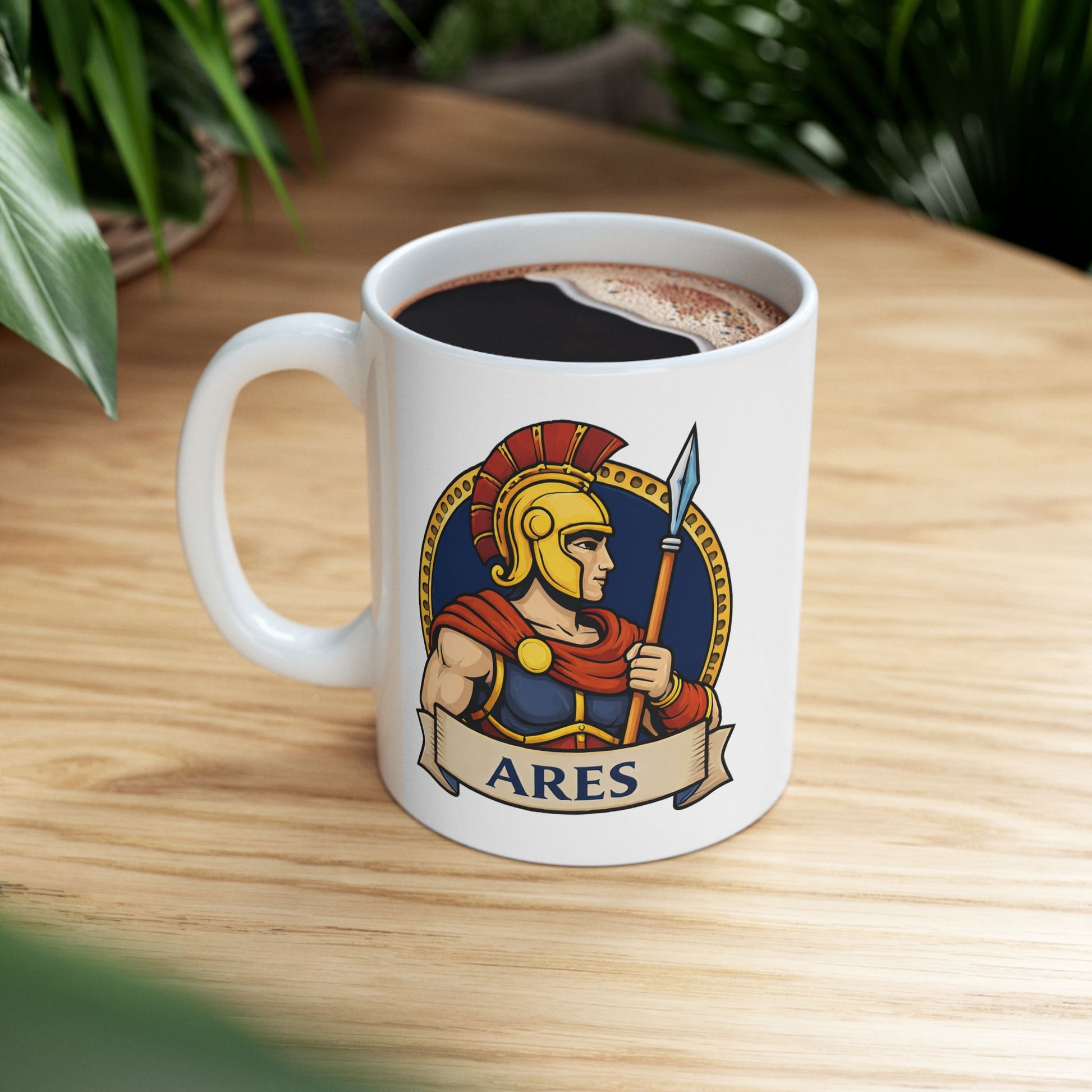 White ceramic mug with a circular emblem of the Greek god Ares in a modern vector art style. He is depicted in profile, wearing a golden Spartan-style helmet with a red crest and a red cape over blue armor. He holds a tall spear against a dark blue background bordered by a gold dotted ring. A tan parchment banner at the bottom displays the name "ARES" in bold, dark blue capital letters.