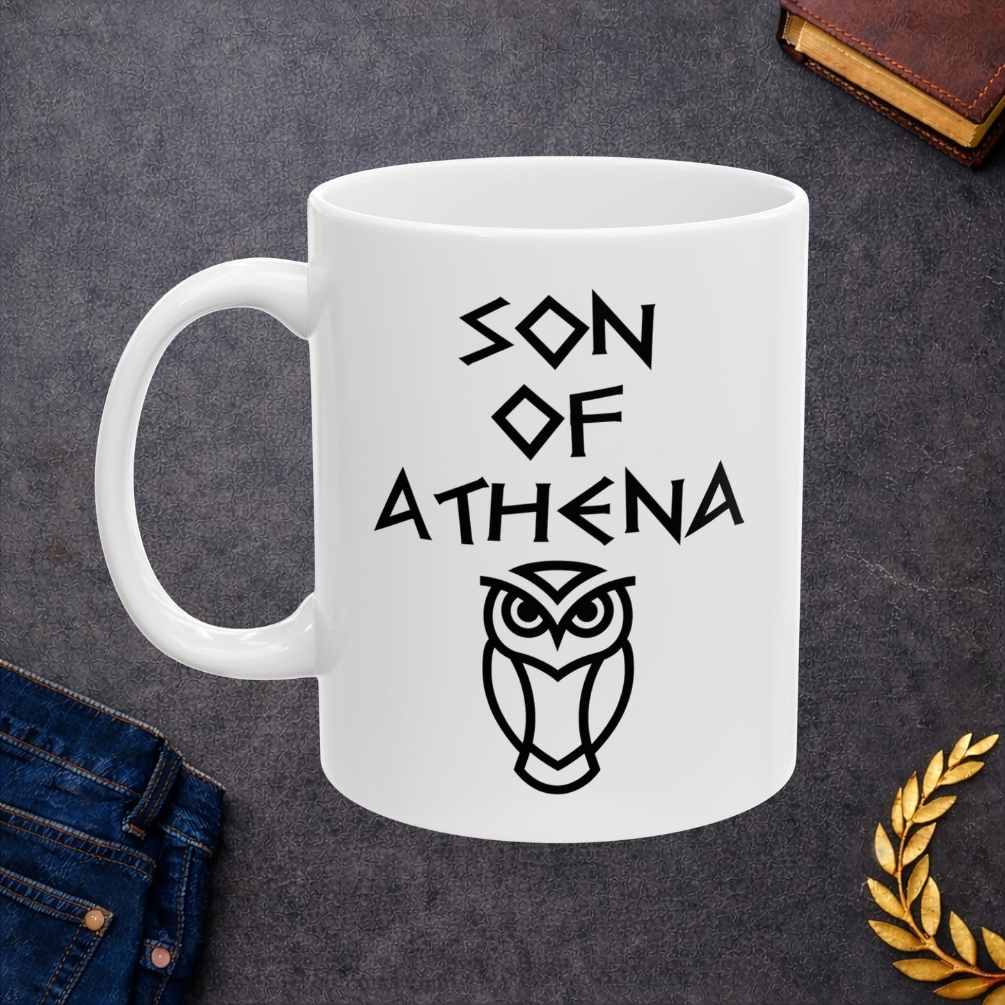 White ceramic mug graphic featuring bold ancient Greek-style lettering reading "Son of Athena" above a clean geometric line-art owl icon — referencing Athena, the Greek Goddess of Wisdom, whose sacred symbol is the owl, rendered in white on black in a striking high-contrast design.