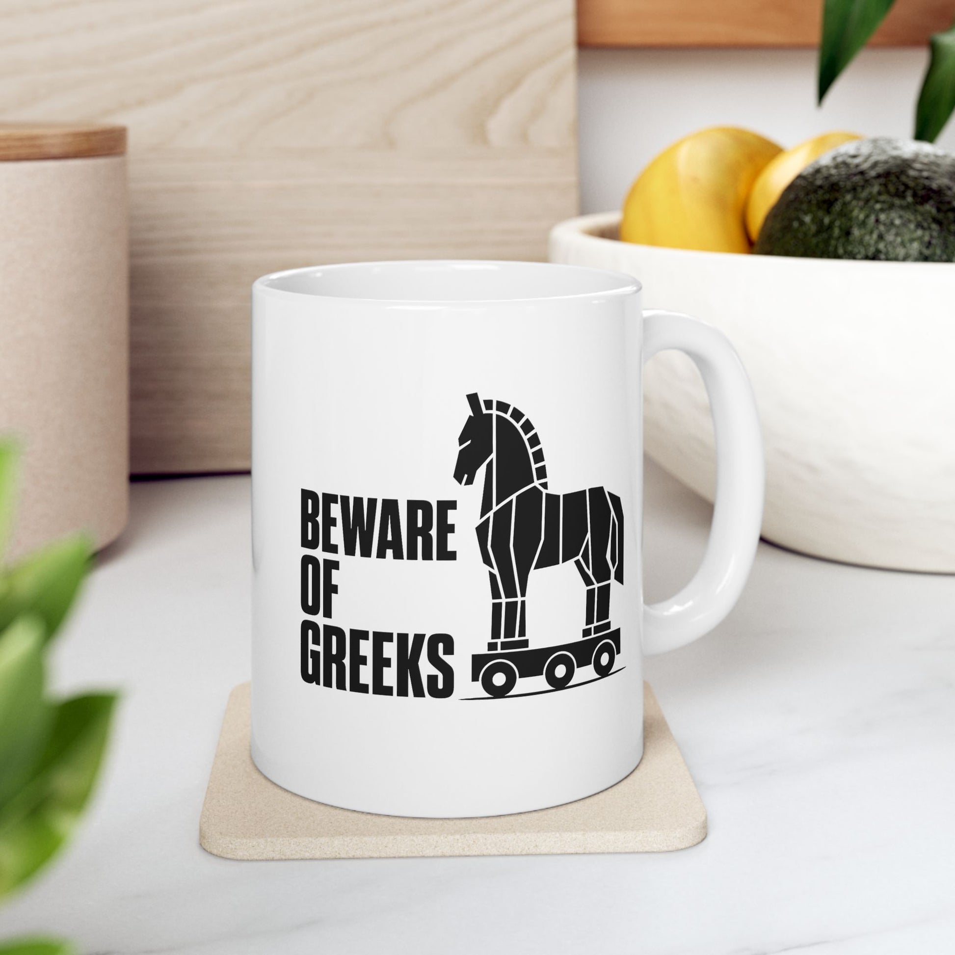 White ceramic mug with a minimalist black-and-white graphic featuring a stylized, geometric silhouette of the Trojan Horse on a wheeled platform. To the left of the horse, the text "BEWARE OF GREEKS" is written vertically in a bold, stacked, black sans-serif font. The design uses clean lines and high contrast on a plain background, offering a modern, minimalist take on the classic Greek mythological tale.