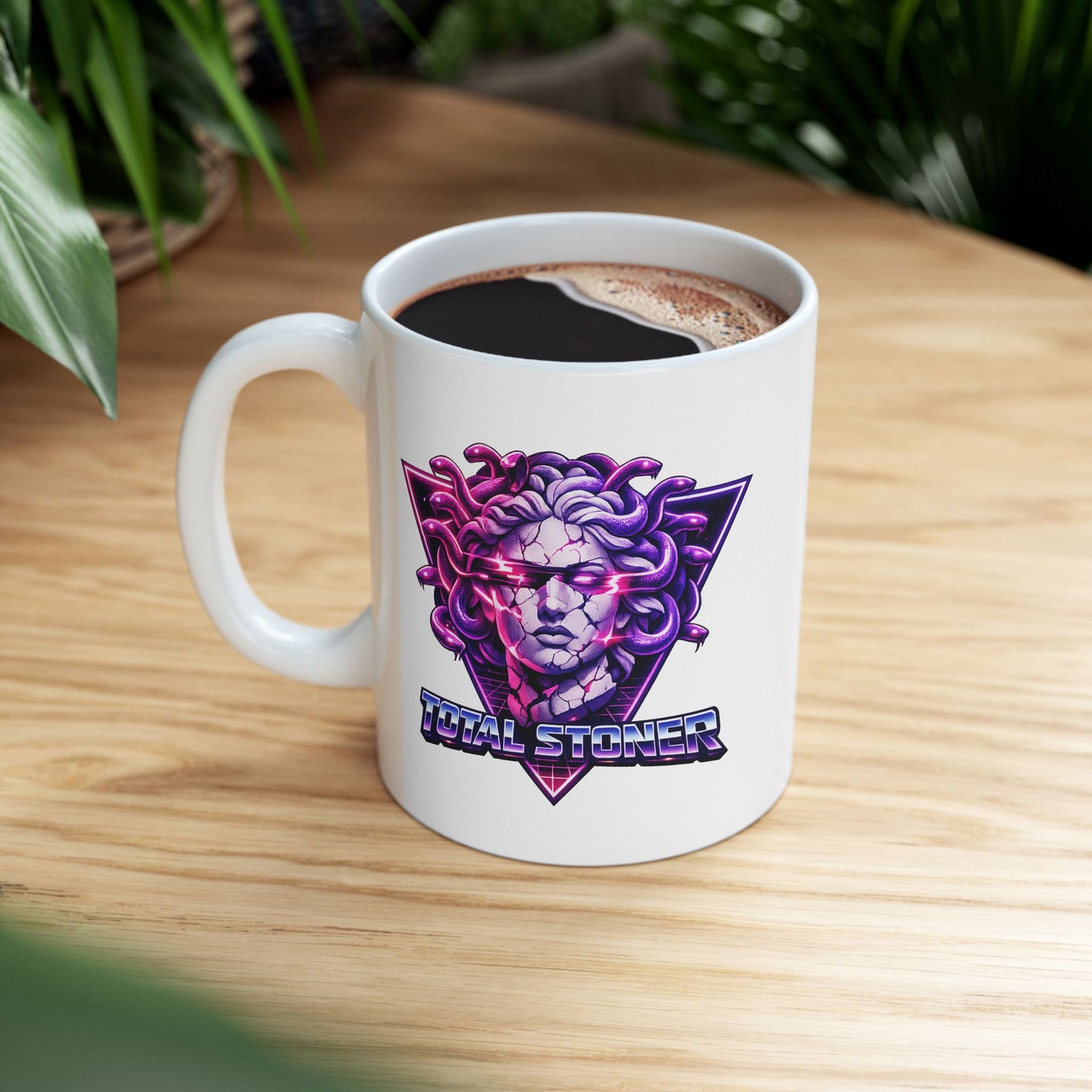White ceramic mug with a synthwave-inspired graphic of Medusa with purple snakes for hair and a cracked stone face. Glowing pink light emanates from her eyes and cracks. The head is centered over a neon pink and purple triangle with a retro grid. Below, the pun "TOTAL STONER" is written in a 1980s-style chrome font with blue and pink gradients. The design uses high-contrast, vibrant neon colors on a dark background.