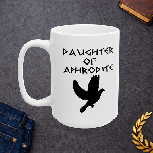 White ceramic mug featuring a minimalist, Greek-inspired graphic in black ink on a white background. The design reads 'DAUGHTER OF APHRODITE' in a stylized, angular font, positioned above a clean, line-art graphic of a dove in flight.
