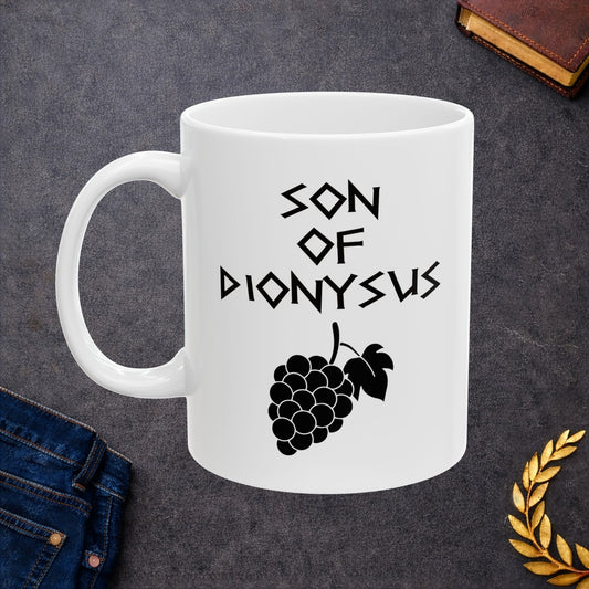 White ceramic mug featuring a minimalist, Greek-inspired graphic in black ink on a white background. The design reads 'SON OF DIONYSUS' in a stylized, angular font, positioned above a clean, line-art graphic of a cluster of grapes hanging from a vine with leaves.