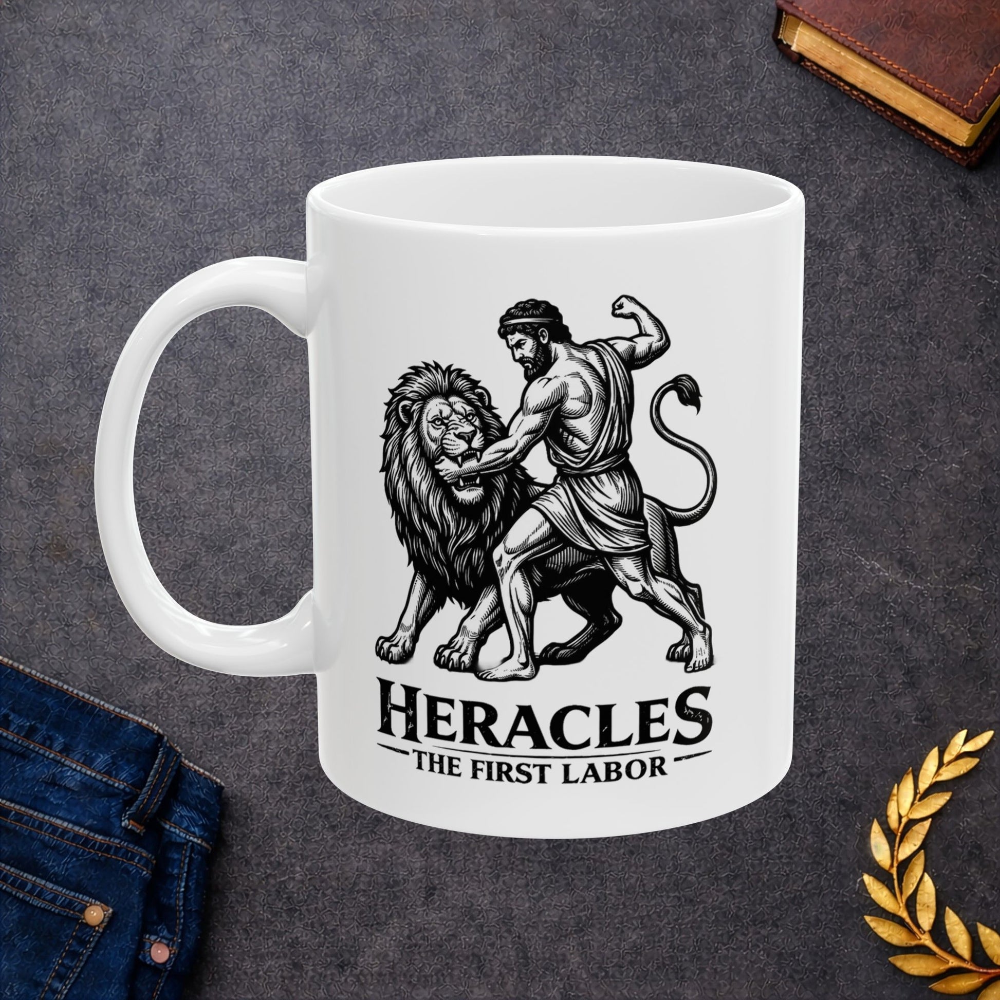 White ceramic mug with a striking black-and-white linocut illustration depicting the Greek hero Heracles wrestling the Nemean Lion. The muscular hero forces his arm into the lion’s open jaws while raising his fist to strike. Below the dynamic scene, bold text reads "HERACLES" followed by a sub-caption that reads "THE FIRST LABOR." The design has a classic, high-contrast vintage woodcut engraving style.