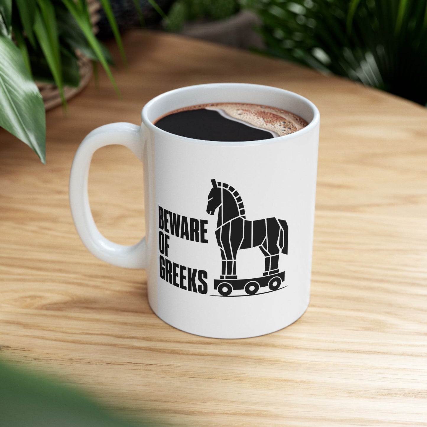 White ceramic mug with a minimalist black-and-white graphic featuring a stylized, geometric silhouette of the Trojan Horse on a wheeled platform. To the left of the horse, the text "BEWARE OF GREEKS" is written vertically in a bold, stacked, black sans-serif font. The design uses clean lines and high contrast on a plain background, offering a modern, minimalist take on the classic Greek mythological tale.