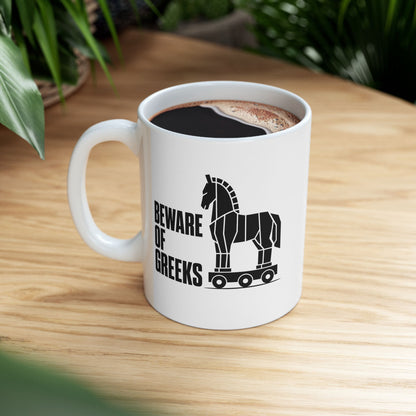 White ceramic mug with a minimalist black-and-white graphic featuring a stylized, geometric silhouette of the Trojan Horse on a wheeled platform. To the left of the horse, the text "BEWARE OF GREEKS" is written vertically in a bold, stacked, black sans-serif font. The design uses clean lines and high contrast on a plain background, offering a modern, minimalist take on the classic Greek mythological tale.