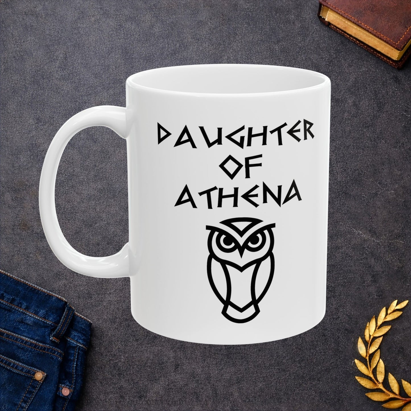 White ceramic mug graphic featuring bold ancient Greek-style lettering reading "Daughter of Athena" above a clean geometric line-art owl icon — referencing Athena, the Greek Goddess of Wisdom, whose sacred symbol is the owl, rendered in white on black in a striking high-contrast design.
