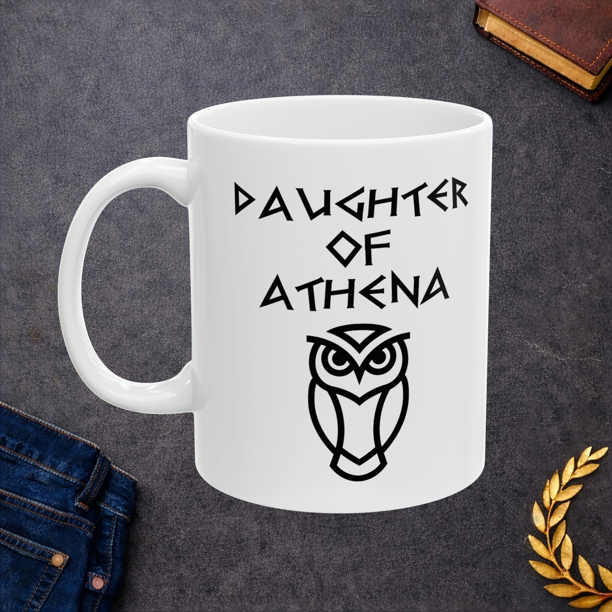 White ceramic mug graphic featuring bold ancient Greek-style lettering reading "Daughter of Athena" above a clean geometric line-art owl icon — referencing Athena, the Greek Goddess of Wisdom, whose sacred symbol is the owl, rendered in white on black in a striking high-contrast design.