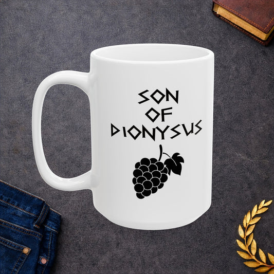 White ceramic mug featuring a minimalist, Greek-inspired graphic in black ink on a white background. The design reads 'SON OF DIONYSUS' in a stylized, angular font, positioned above a clean, line-art graphic of a cluster of grapes hanging from a vine with leaves.