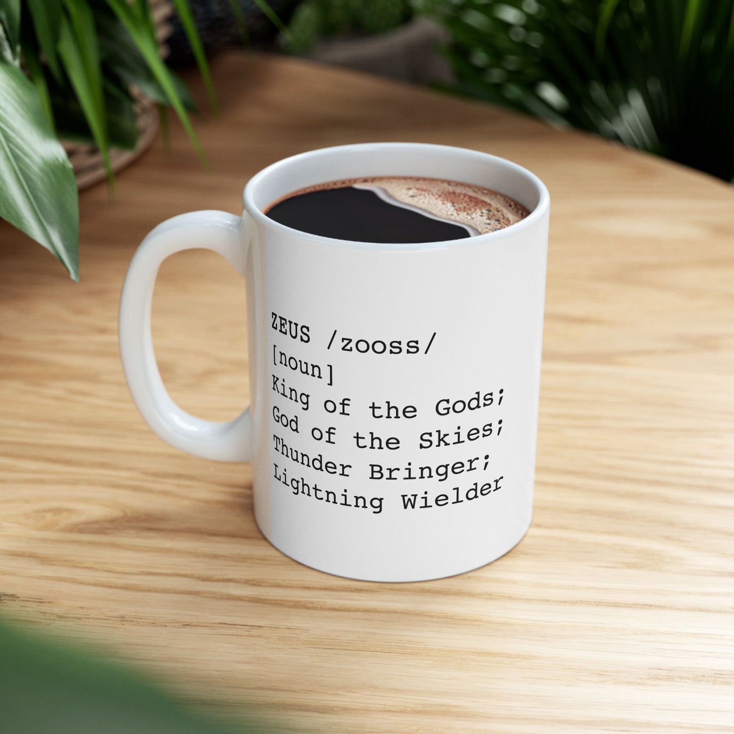 A minimalist black graphic for a white ceramic mug, styled as a dictionary entry. The design features the name "ZEUS" in a bold typewriter font, followed by the phonetic pronunciation "/zooss/," the word class "[noun]," and the definition: "King of the Gods; God of the Skies; Thunder Bringer; Lightning Wielder.