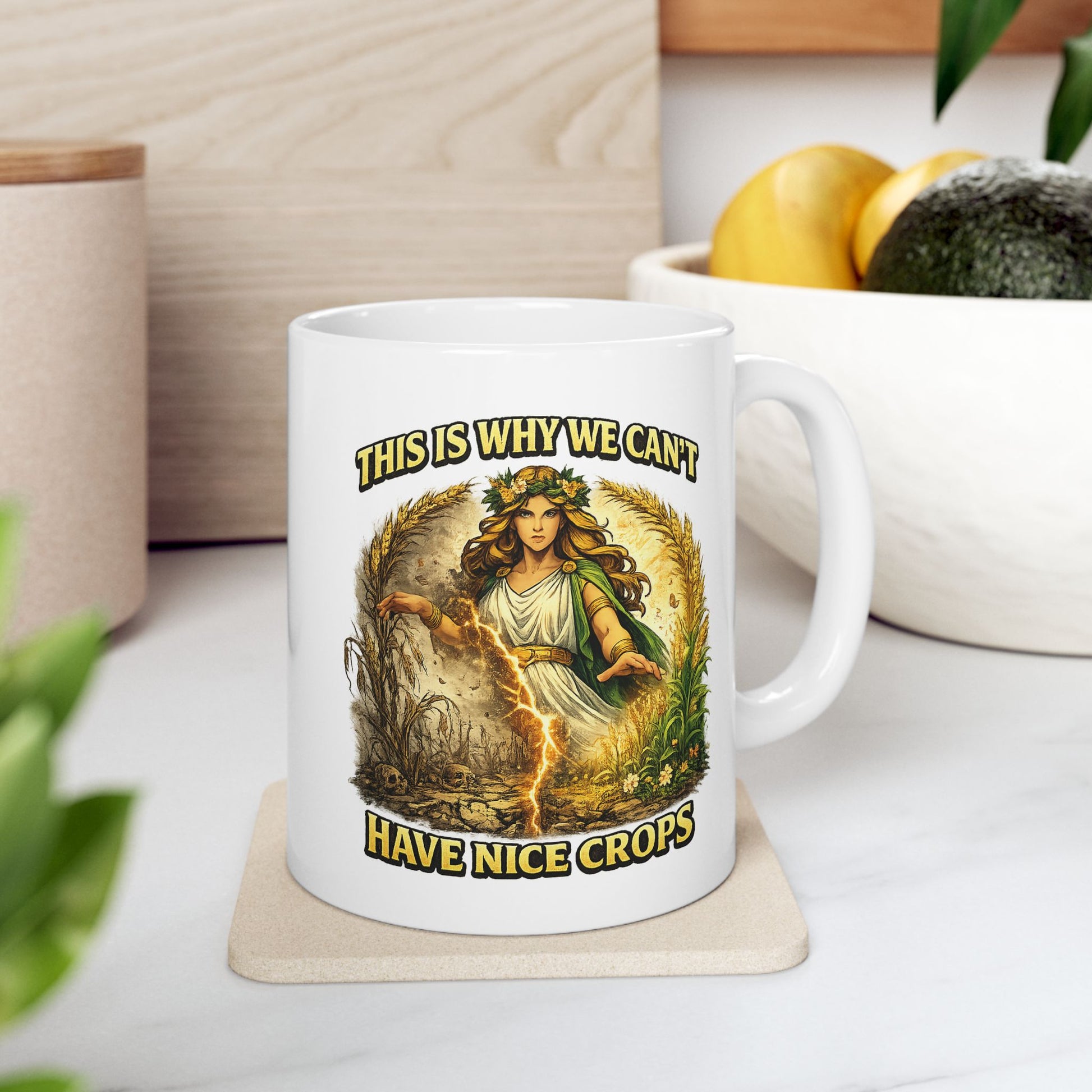 White ceramic mug with a dramatic illustration of Demeter, the Greek goddess of agriculture, standing over a split field. A glowing lightning strike cracks down the center, dividing flourishing, green crops on the right from dead, withered stalks and skulls on the left. Arching text above and below reads "THIS IS WHY WE CAN'T HAVE NICE CROPS" in a bold, weathered yellow font. The design has an intense, mythical comic art style.