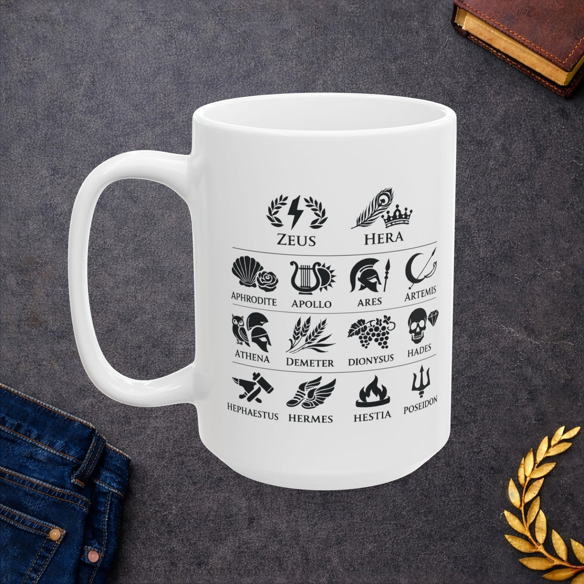 White ceramic mug with a Greek mythology gods icon chart featuring symbolic illustrations for Zeus, Hera, Aphrodite, Apollo, Ares, Artemis, Athena, Demeter, Dionysus, Hades, Hephaestus, Hermes, Hestia, and Poseidon. Black icons include lightning, peacock feather, rose, lyre, helmet, bow, owl, wheat, grapes, skull, anvil, winged sandals, flame, and trident.