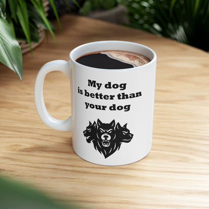 White ceramic mug with a minimalist black-and-white graphic featuring a bold, three-headed Cerberus illustration. The hound of the underworld is shown with snarling expressions and sharp teeth. Above the heads, the phrase "My dog is better than your dog" is written in a heavy, black slab-serif font. The design is a clean, modern take on Greek mythology with a humorous twist.