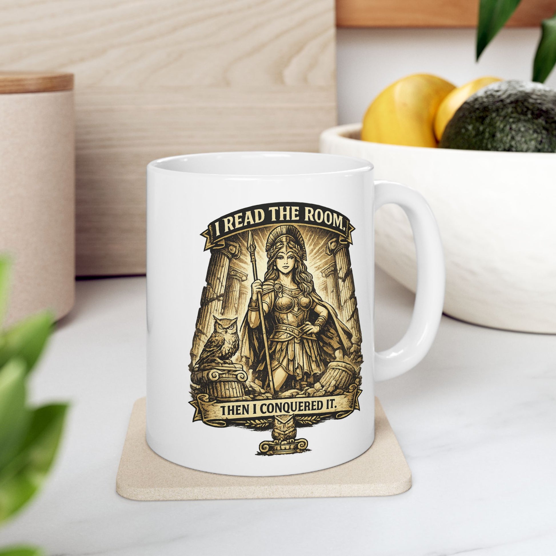 White ceramic mug with a detailed sepia-toned illustration of the goddess Athena in battle armor, holding a spear among ruined Greek columns. An owl perches on a pedestal beside her. Banners above and below read "I READ THE ROOM" and "THEN I CONQUERED IT." The design features an intricate, etched vintage style with classical motifs, combining a modern empowering slogan with ancient Greek aesthetics.