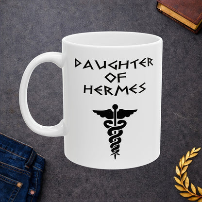 A minimalist black graphic for a white ceramic mug featuring a central caduceus symbol—a winged staff with two snakes entwined around it. Above the symbol, the text "DAUGHTER OF HERMES" is displayed in a sharp, angular font inspired by ancient Greek stone carvings. The entire design is rendered in a clean, high-contrast black outline.