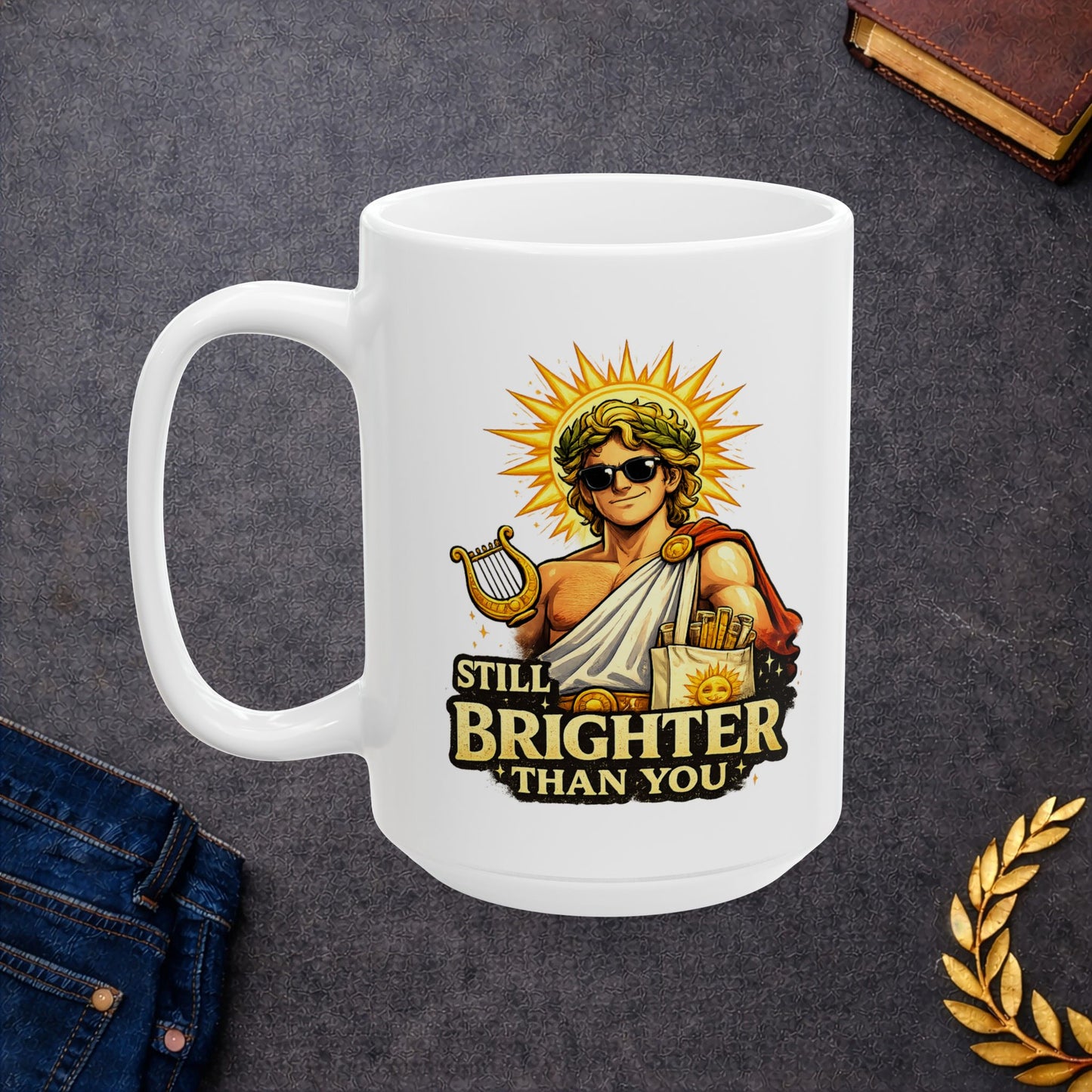 White ceramic mug with a humorous, vibrant illustration of the Greek god Apollo wearing dark sunglasses and a laurel wreath, with a glowing golden sunburst behind his head. He holds a golden lyre and wears a toga with a red cape. Below the smirking god, the cheeky text reads "STILL BRIGHTER THAN YOU" in a bold, weathered yellow font.