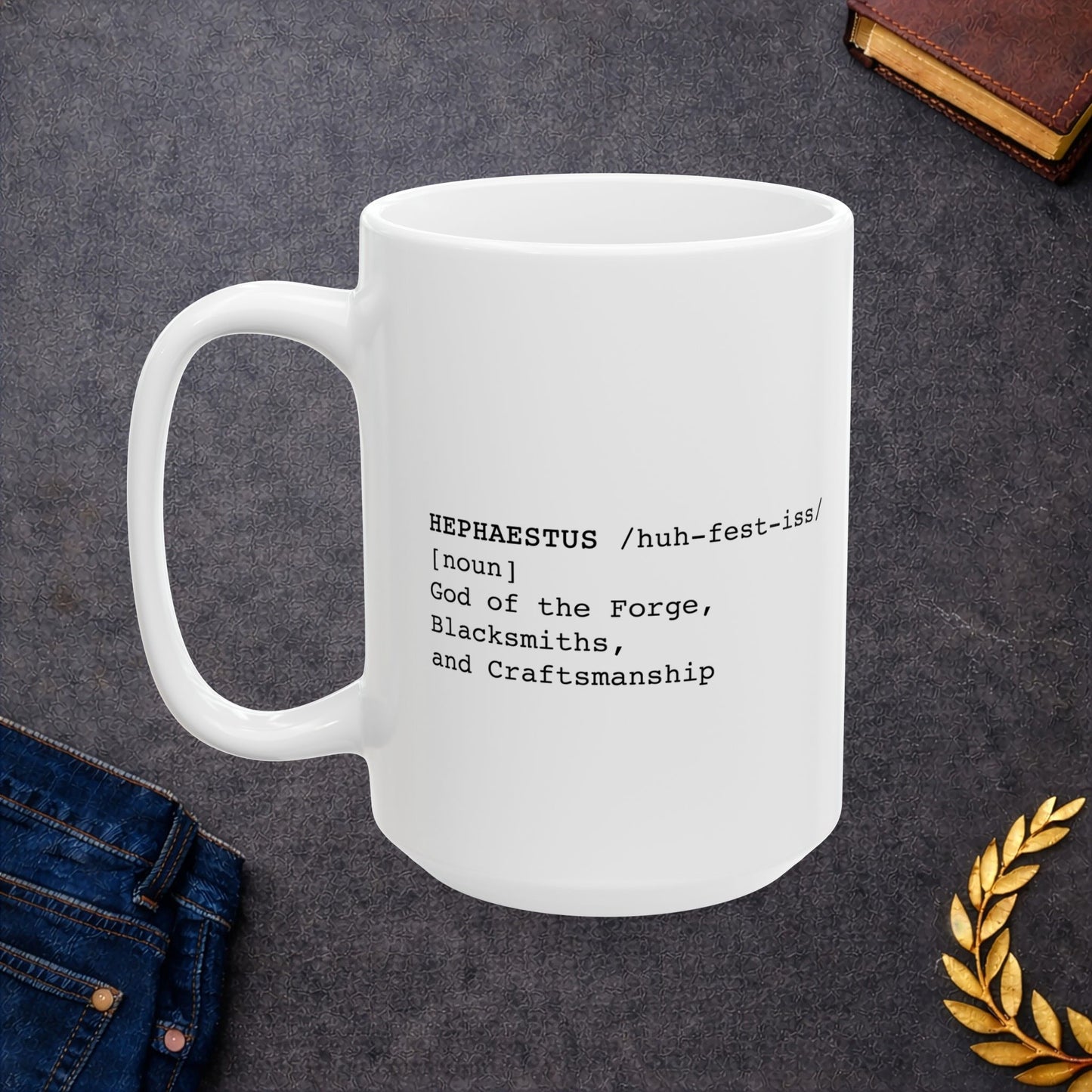A minimalist black-on-white graphic for a ceramic mug, styled as a dictionary entry. The text features the name "HEPHAESTUS" in a bold typewriter font, followed by the phonetic pronunciation "/huh-fest-iss/," the word class "[noun]," and the definition: "God of the Forge, Blacksmiths, and Craftsmanship.