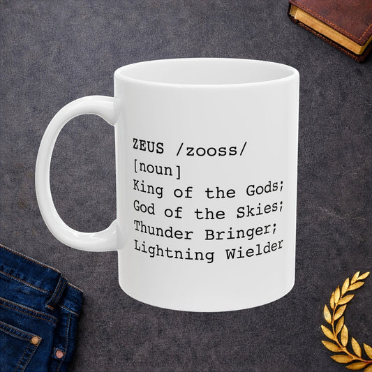 A minimalist black graphic for a white ceramic mug, styled as a dictionary entry. The design features the name "ZEUS" in a bold typewriter font, followed by the phonetic pronunciation "/zooss/," the word class "[noun]," and the definition: "King of the Gods; God of the Skies; Thunder Bringer; Lightning Wielder.