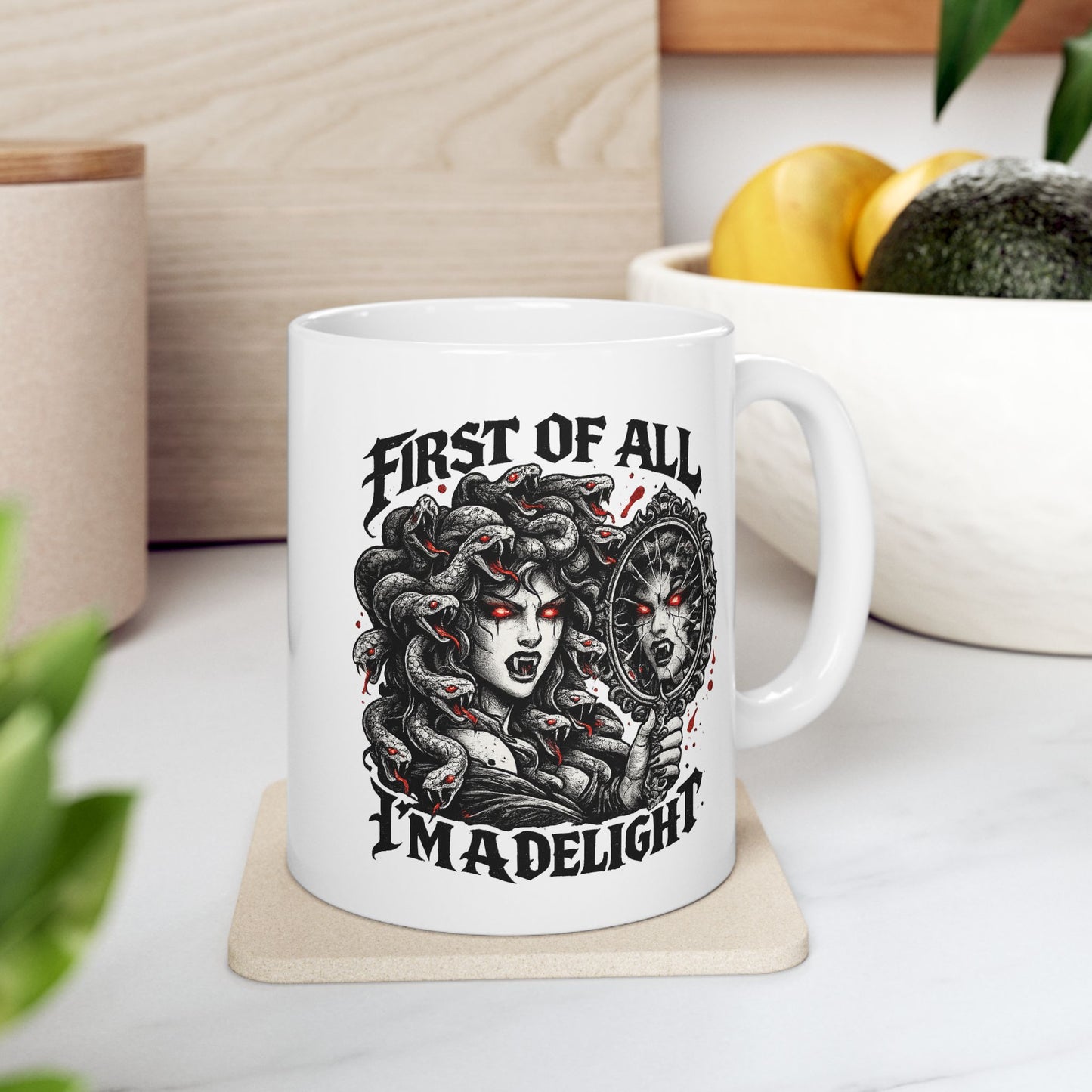 Gothic streetwear illustration of Medusa on a ceramic white mug. Black and white engraving features the figure with serpents for hair, each snake with glowing red eyes. She holds an ornate mirror reflecting her fierce expression with matching red-eyed gaze. Text reads 'First of All, I'm A Delight' in bold metal lettering. Red accents highlight the snakes' eyes. Clever wordplay blends mythology with modern sarcastic humor and confidence.