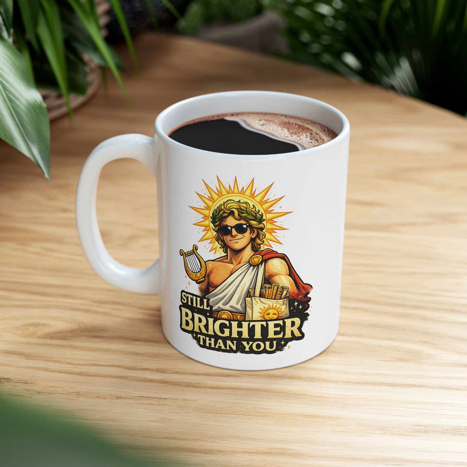White ceramic mug with a humorous, vibrant illustration of the Greek god Apollo wearing dark sunglasses and a laurel wreath, with a glowing golden sunburst behind his head. He holds a golden lyre and wears a toga with a red cape. Below the smirking god, the cheeky text reads "STILL BRIGHTER THAN YOU" in a bold, weathered yellow font.