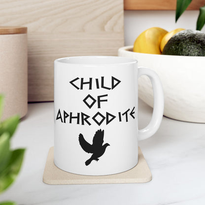 White ceramic mug featuring a minimalist, Greek-inspired graphic in black ink on a white background. The design reads 'CHILD OF APHRODITE' in a stylized, angular font, positioned above a clean, line-art graphic of a dove in flight.