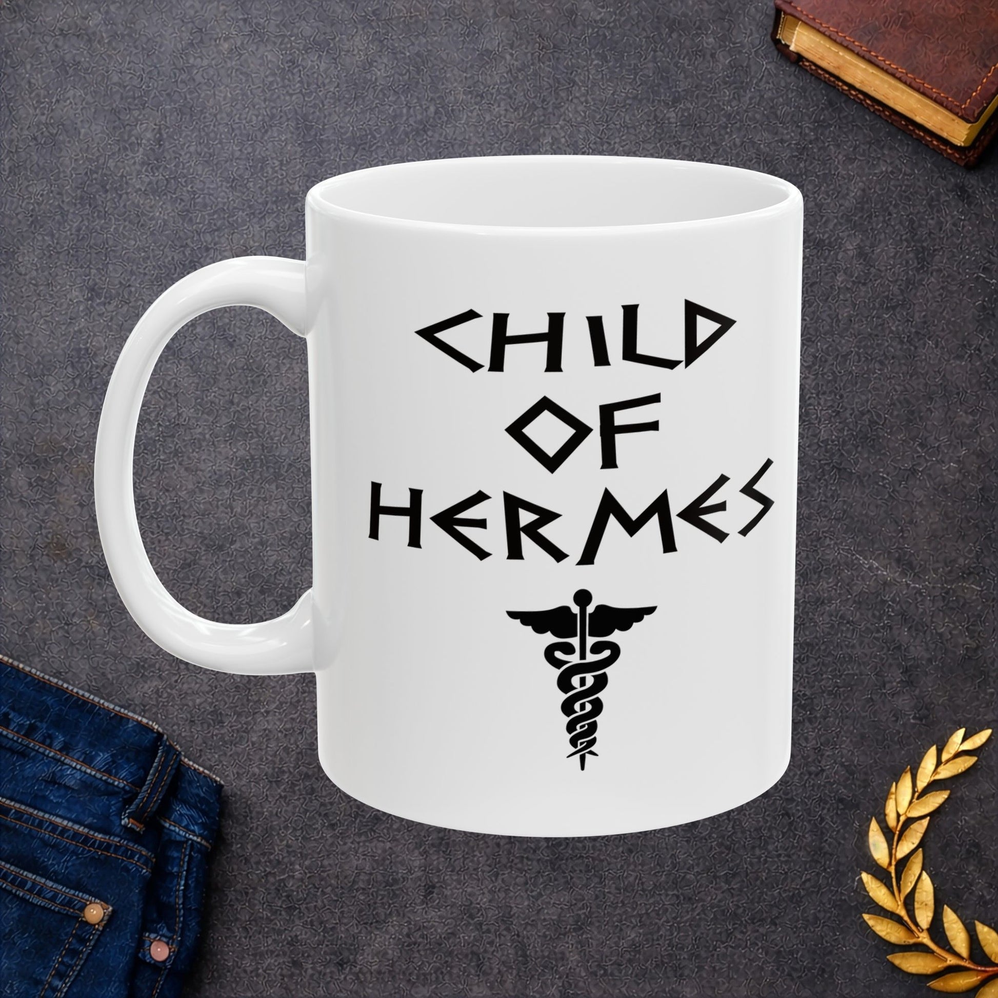 A minimalist black graphic for a white ceramic mug featuring a central caduceus symbol—a winged staff with two snakes entwined around it. Above the symbol, the text "CHILD OF HERMES" is displayed in a sharp, angular font inspired by ancient Greek stone carvings. The entire design is rendered in a clean, high-contrast black outline.