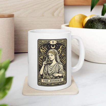 White ceramic mug with a gold and black tarot card-style illustration titled "THE AVOIDER," featuring Hestia from Greek mythology. It depicts the goddess in serene draped robes calmly sipping from a steaming cup, staying unfazed by a chaotic background of stormy clouds, lightning bolts, and tridents. The card includes ornate borders, a crescent moon, and the Roman numeral "II" at the top, creating a humorous, mystical aesthetic.