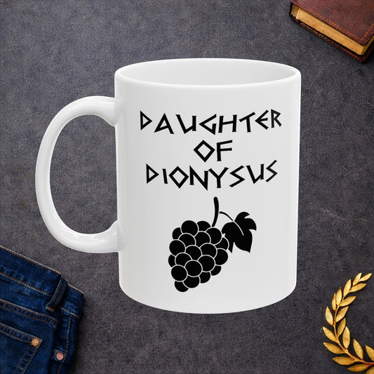 White ceramic mug featuring a minimalist, Greek-inspired graphic in black ink on a white background. The design reads 'DAUGHTER OF DIONYSUS' in a stylized, angular font, positioned above a clean, line-art graphic of a cluster of grapes hanging from a vine with leaves.