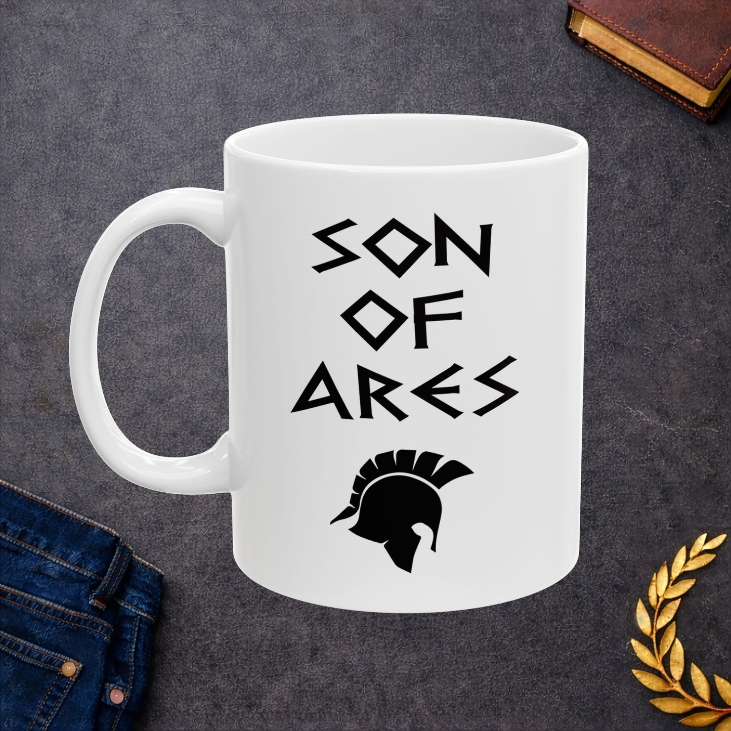 White ceramic mug featuring a minimalist, Greek-inspired graphic in black ink on a white background. The design reads 'SON OF ARES' in a stylized, angular font, positioned above a clean, line-art graphic of a Spartan-style plumed warrior helmet.