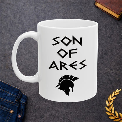 White ceramic mug featuring a minimalist, Greek-inspired graphic in black ink on a white background. The design reads 'SON OF ARES' in a stylized, angular font, positioned above a clean, line-art graphic of a Spartan-style plumed warrior helmet.