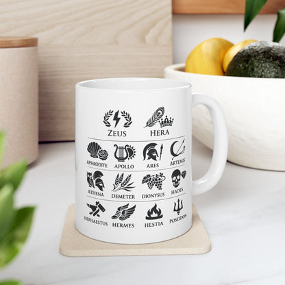 White ceramic mug with a Greek mythology gods icon chart featuring symbolic illustrations for Zeus, Hera, Aphrodite, Apollo, Ares, Artemis, Athena, Demeter, Dionysus, Hades, Hephaestus, Hermes, Hestia, and Poseidon. Black icons include lightning, peacock feather, rose, lyre, helmet, bow, owl, wheat, grapes, skull, anvil, winged sandals, flame, and trident.