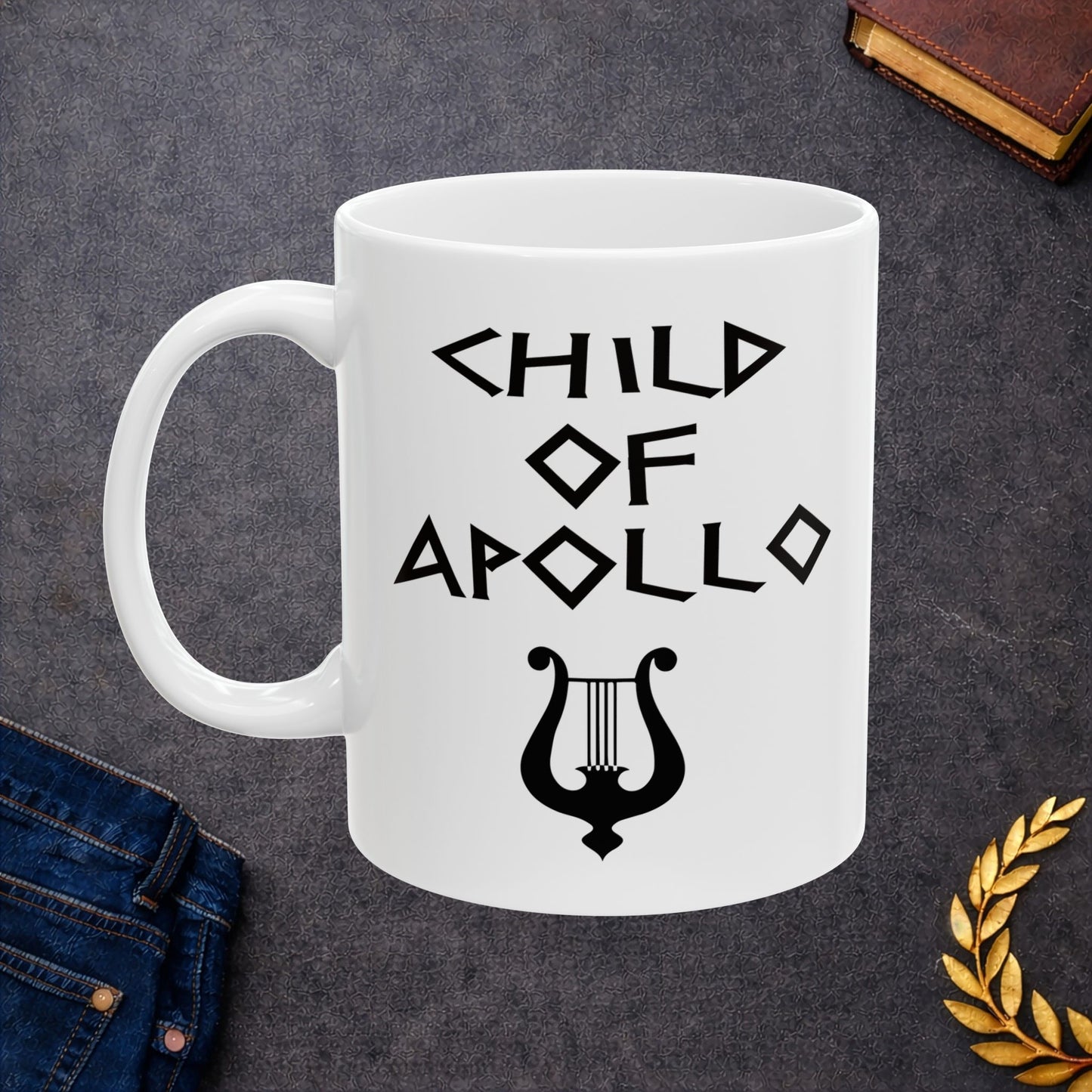 White ceramic mug featuring a minimalist, Greek-inspired graphic in black ink on a white background. The design reads 'CHILD OF APOLLO' in a stylized, angular font, positioned above a clean, line-art graphic of a classical lyre.