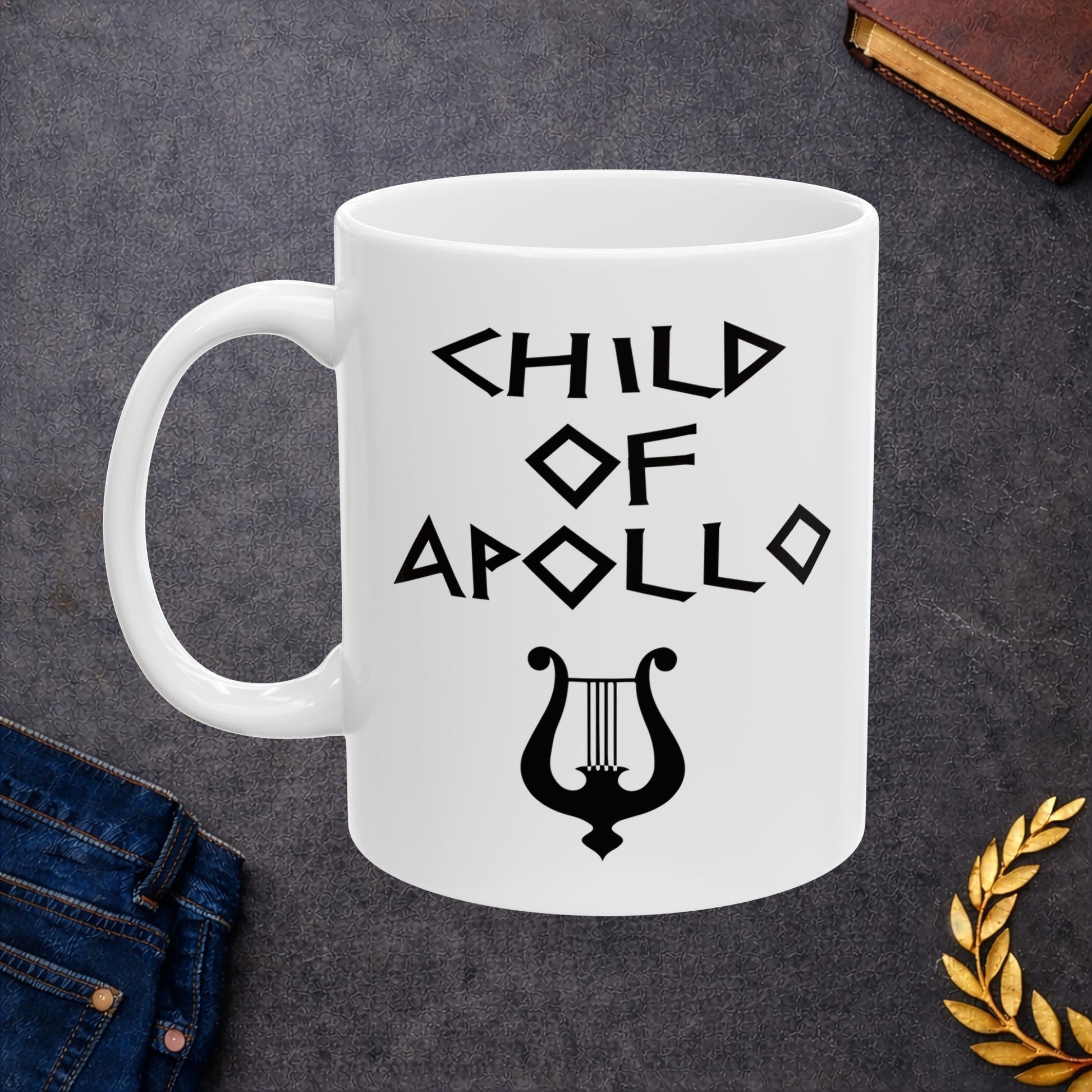 White ceramic mug featuring a minimalist, Greek-inspired graphic in black ink on a white background. The design reads 'CHILD OF APOLLO' in a stylized, angular font, positioned above a clean, line-art graphic of a classical lyre.