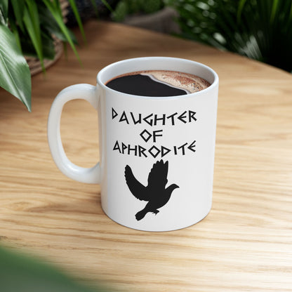 White ceramic mug featuring a minimalist, Greek-inspired graphic in black ink on a white background. The design reads 'DAUGHTER OF APHRODITE' in a stylized, angular font, positioned above a clean, line-art graphic of a dove in flight.