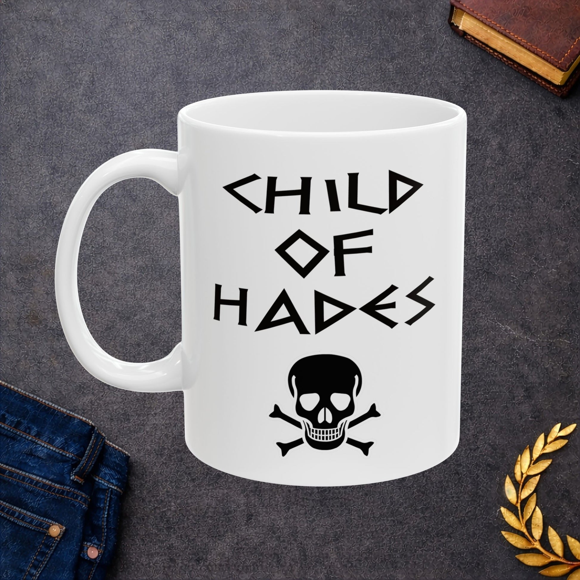A bold, dark-themed graphic for a white ceramic mug. The design features a large, detailed outline of a skull and crossbones at the center. Above the skull, the words "CHILD OF HADES" are written in a sharp, ancient Greek-inspired angular font. The entire design is rendered in a clean, high-contrast black outline style.
