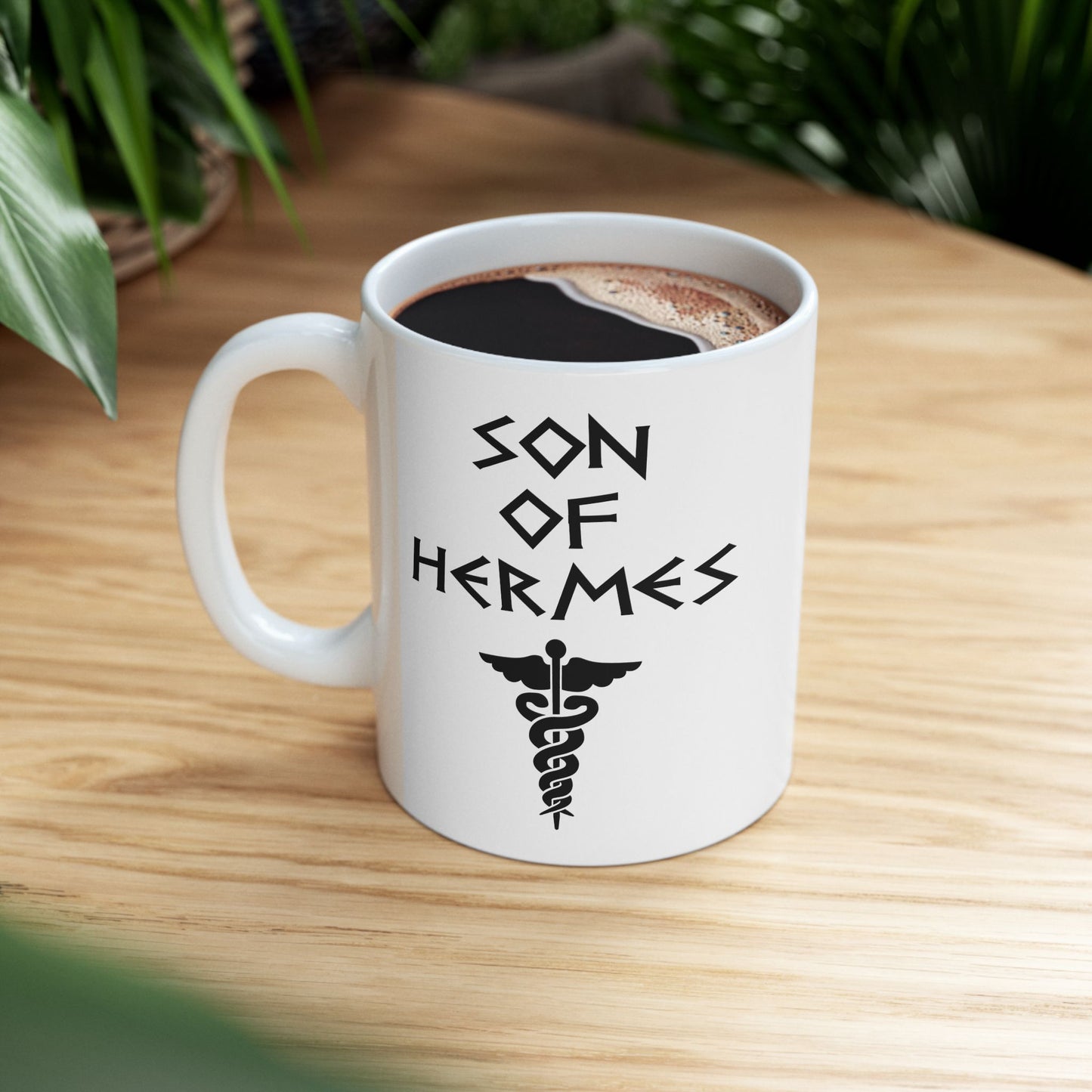 A minimalist black graphic for a white ceramic mug featuring a central caduceus symbol—a winged staff with two snakes entwined around it. Above the symbol, the text "SON OF HERMES" is displayed in a sharp, angular font inspired by ancient Greek stone carvings. The entire design is rendered in a clean, high-contrast black outline.