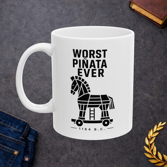 White ceramic mug with a minimalist black-and-white graphic featuring a stylized, geometric silhouette of the Trojan Horse on a wheeled platform with a small ladder underneath. Stacked above the horse, bold black text reads "WORST PIÑATA EVER." Centered below the wheels, a sub-caption reads "— 1184 B.C. —" framed by thin horizontal lines. The clean, high-contrast design offers a humorous, modern take on the ancient Greek myth.
