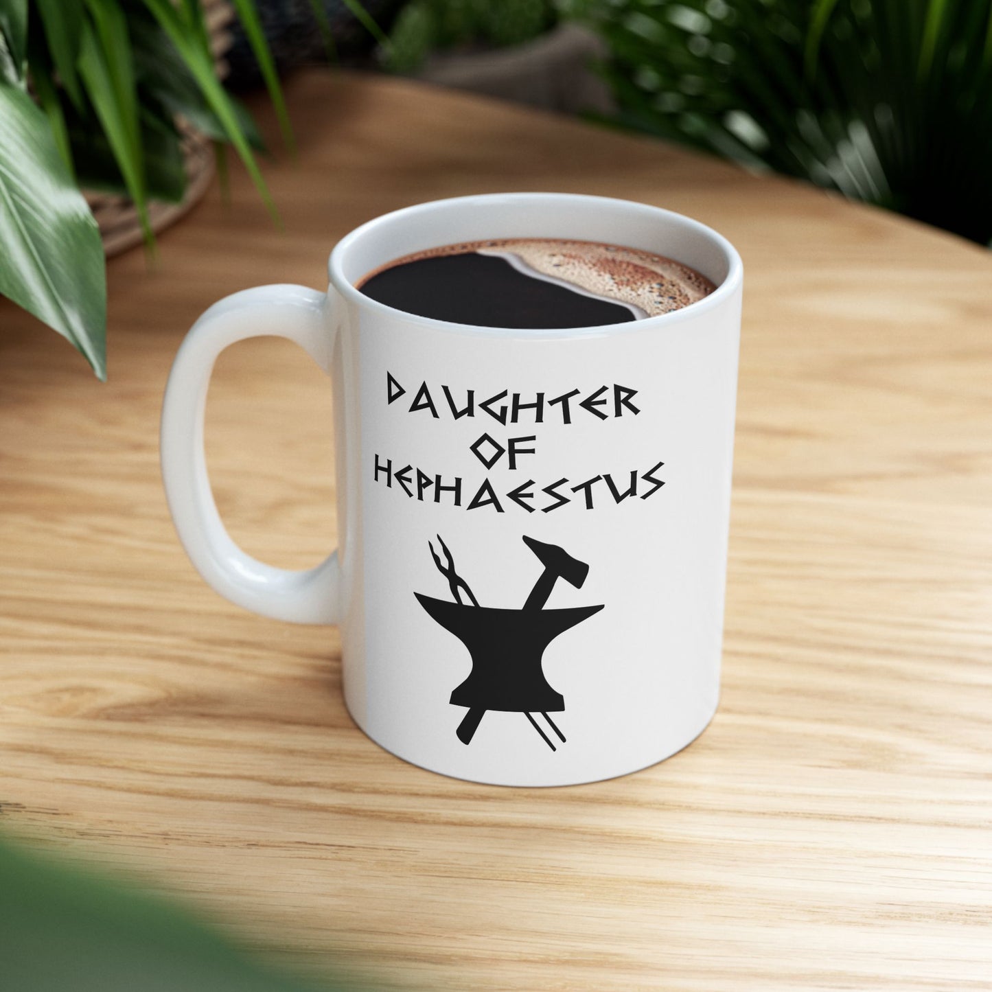 A minimalist black graphic for a white ceramic mug. The design features a central silhouette of a blacksmith's anvil with a hammer and tongs crossed behind it. Above the tools, the text "DAUGHTER OF HEPHAESTUS" is written in a sharp, angular font inspired by ancient Greek inscriptions. The entire illustration is rendered in a clean, solid black style.