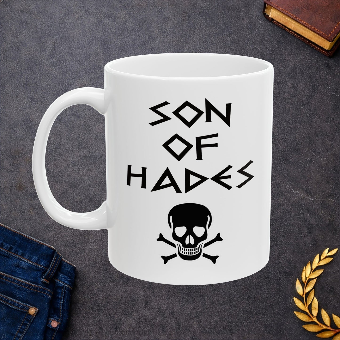 A bold, dark-themed graphic for a white ceramic mug. The design features a large, detailed outline of a skull and crossbones at the center. Above the skull, the words "SON OF HADES" are written in a sharp, ancient Greek-inspired angular font. The entire design is rendered in a clean, high-contrast black outline style.