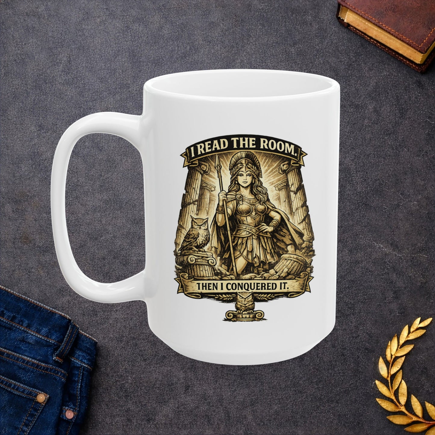 White ceramic mug with a detailed sepia-toned illustration of the goddess Athena in battle armor, holding a spear among ruined Greek columns. An owl perches on a pedestal beside her. Banners above and below read "I READ THE ROOM" and "THEN I CONQUERED IT." The design features an intricate, etched vintage style with classical motifs, combining a modern empowering slogan with ancient Greek aesthetics.