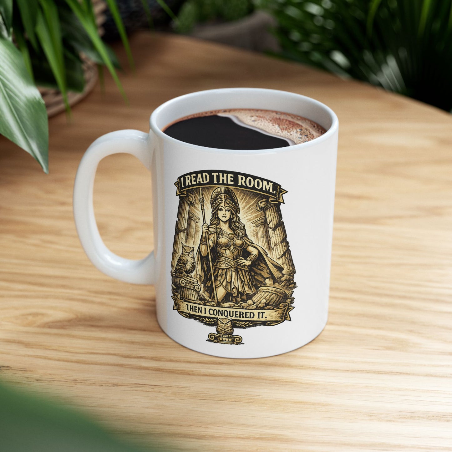 White ceramic mug with a detailed sepia-toned illustration of the goddess Athena in battle armor, holding a spear among ruined Greek columns. An owl perches on a pedestal beside her. Banners above and below read "I READ THE ROOM" and "THEN I CONQUERED IT." The design features an intricate, etched vintage style with classical motifs, combining a modern empowering slogan with ancient Greek aesthetics.