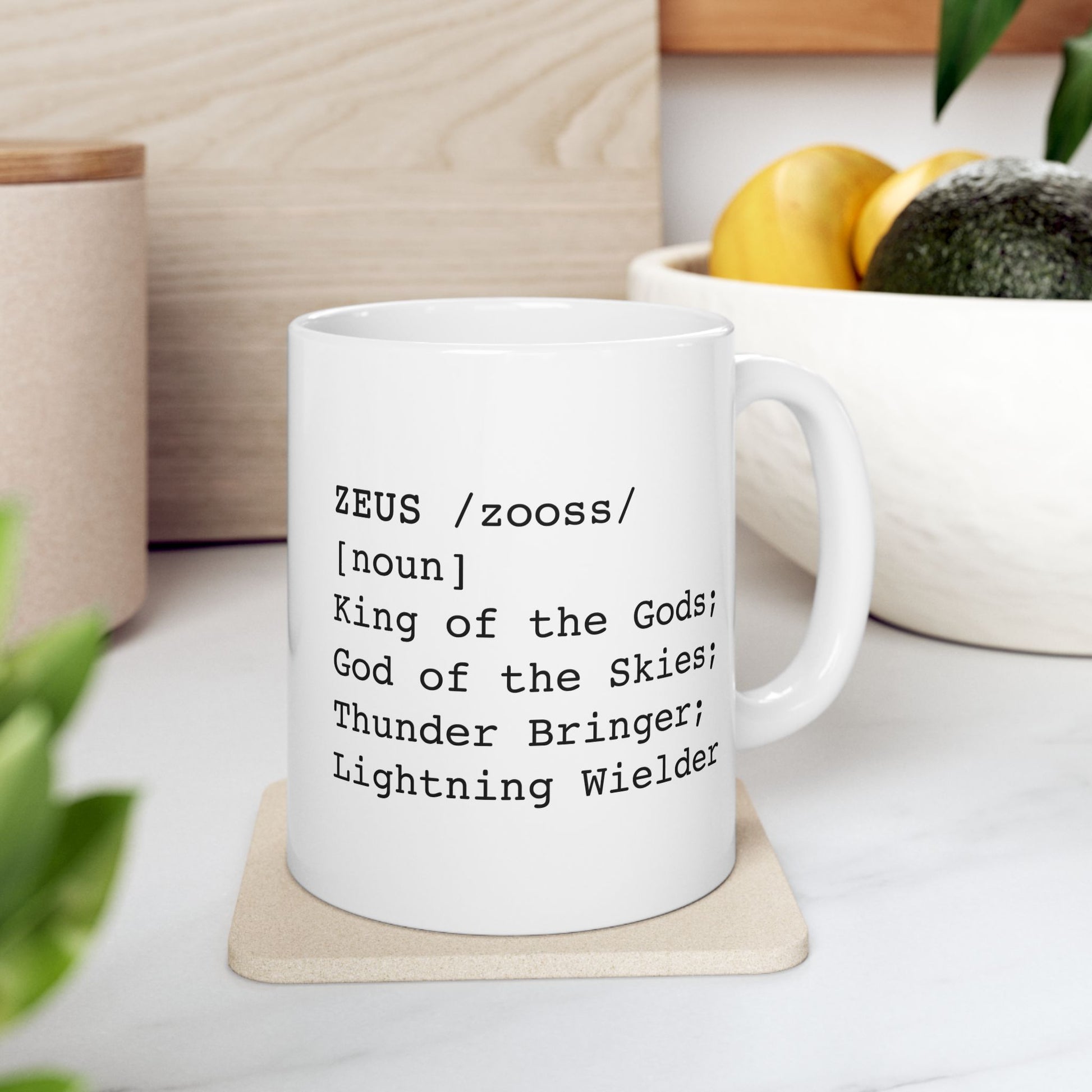 A minimalist black graphic for a white ceramic mug, styled as a dictionary entry. The design features the name "ZEUS" in a bold typewriter font, followed by the phonetic pronunciation "/zooss/," the word class "[noun]," and the definition: "King of the Gods; God of the Skies; Thunder Bringer; Lightning Wielder.