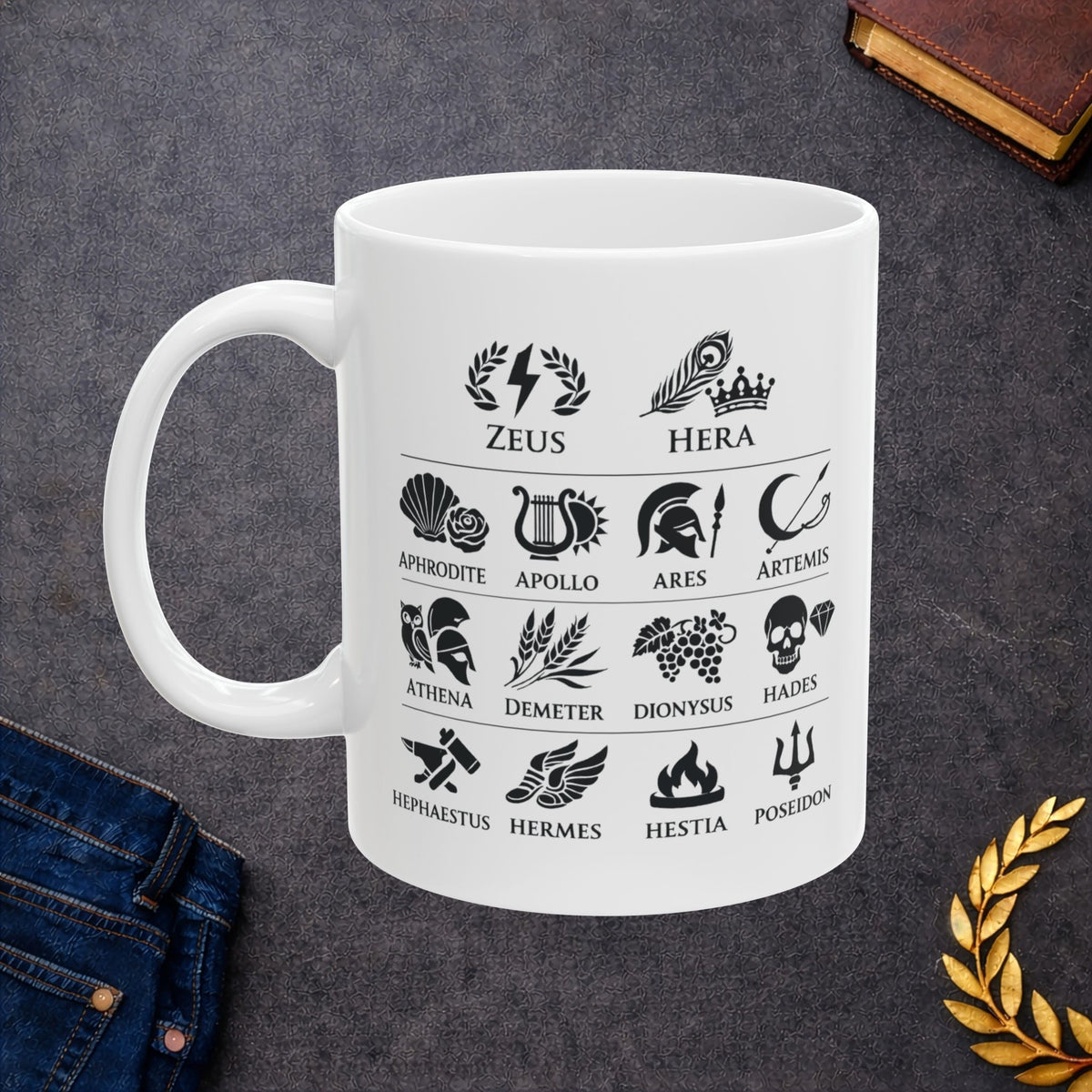 White ceramic mug with a Greek mythology gods icon chart featuring symbolic illustrations for Zeus, Hera, Aphrodite, Apollo, Ares, Artemis, Athena, Demeter, Dionysus, Hades, Hephaestus, Hermes, Hestia, and Poseidon. Black icons include lightning, peacock feather, rose, lyre, helmet, bow, owl, wheat, grapes, skull, anvil, winged sandals, flame, and trident.