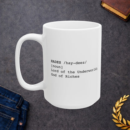 A minimalist graphic for a white ceramic mug featuring black typewriter-style text. The design is formatted like a dictionary entry for "HADES," including the phonetic pronunciation "/hay-deez/," the word class "[noun]," and the definition: "Lord of the Underworld; God of Riches.