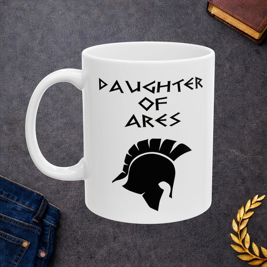 White ceramic mug featuring a minimalist, Greek-inspired graphic in black ink on a white background. The design reads 'DAUGHTER OF ARES' in a stylized, angular font, positioned above a clean, line-art graphic of a Spartan-style plumed warrior helmet.