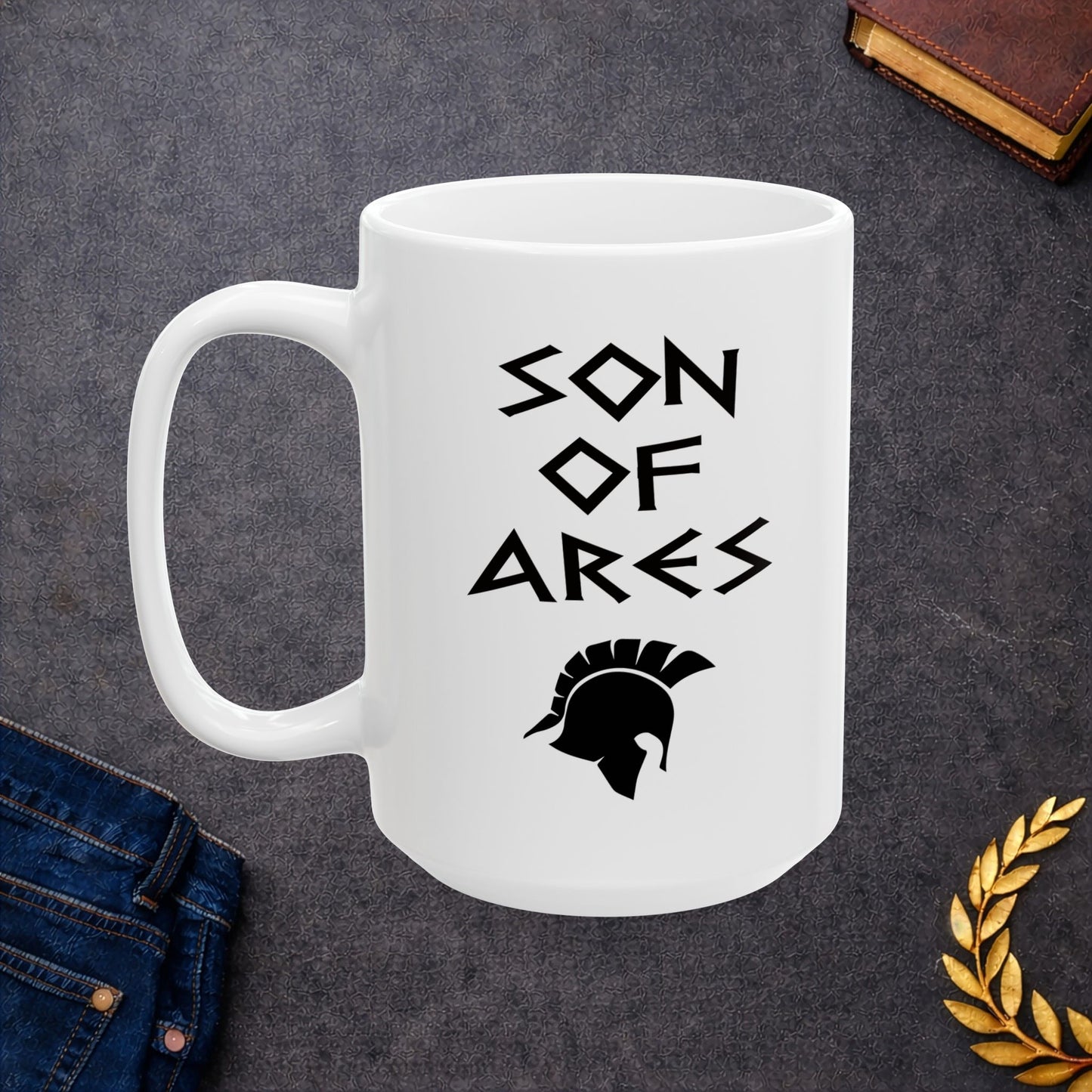 White ceramic mug featuring a minimalist, Greek-inspired graphic in black ink on a white background. The design reads 'SON OF ARES' in a stylized, angular font, positioned above a clean, line-art graphic of a Spartan-style plumed warrior helmet.