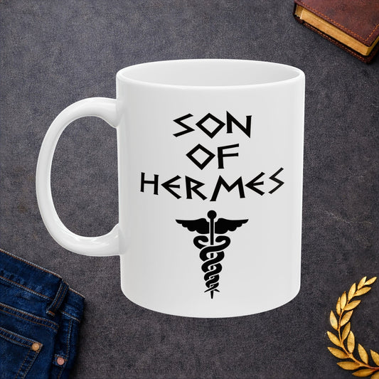 A minimalist black graphic for a white ceramic mug featuring a central caduceus symbol—a winged staff with two snakes entwined around it. Above the symbol, the text "SON OF HERMES" is displayed in a sharp, angular font inspired by ancient Greek stone carvings. The entire design is rendered in a clean, high-contrast black outline.