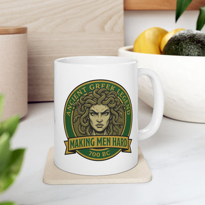 Funny Greek mythology mug design featuring a bold vintage badge with Medusa's stern face surrounded by writhing snakes. The circular emblem reads "Ancient Greek Legend" across the top and "Making Men Hard" on a banner below, with "700 BC" at the bottom. The design uses classic green, gold, and olive tones in a retro emblem style, combining mythology with humorous wordplay.