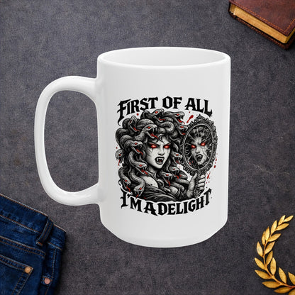Gothic streetwear illustration of Medusa on a ceramic white mug. Black and white engraving features the figure with serpents for hair, each snake with glowing red eyes. She holds an ornate mirror reflecting her fierce expression with matching red-eyed gaze. Text reads 'First of All, I'm A Delight' in bold metal lettering. Red accents highlight the snakes' eyes. Clever wordplay blends mythology with modern sarcastic humor and confidence.