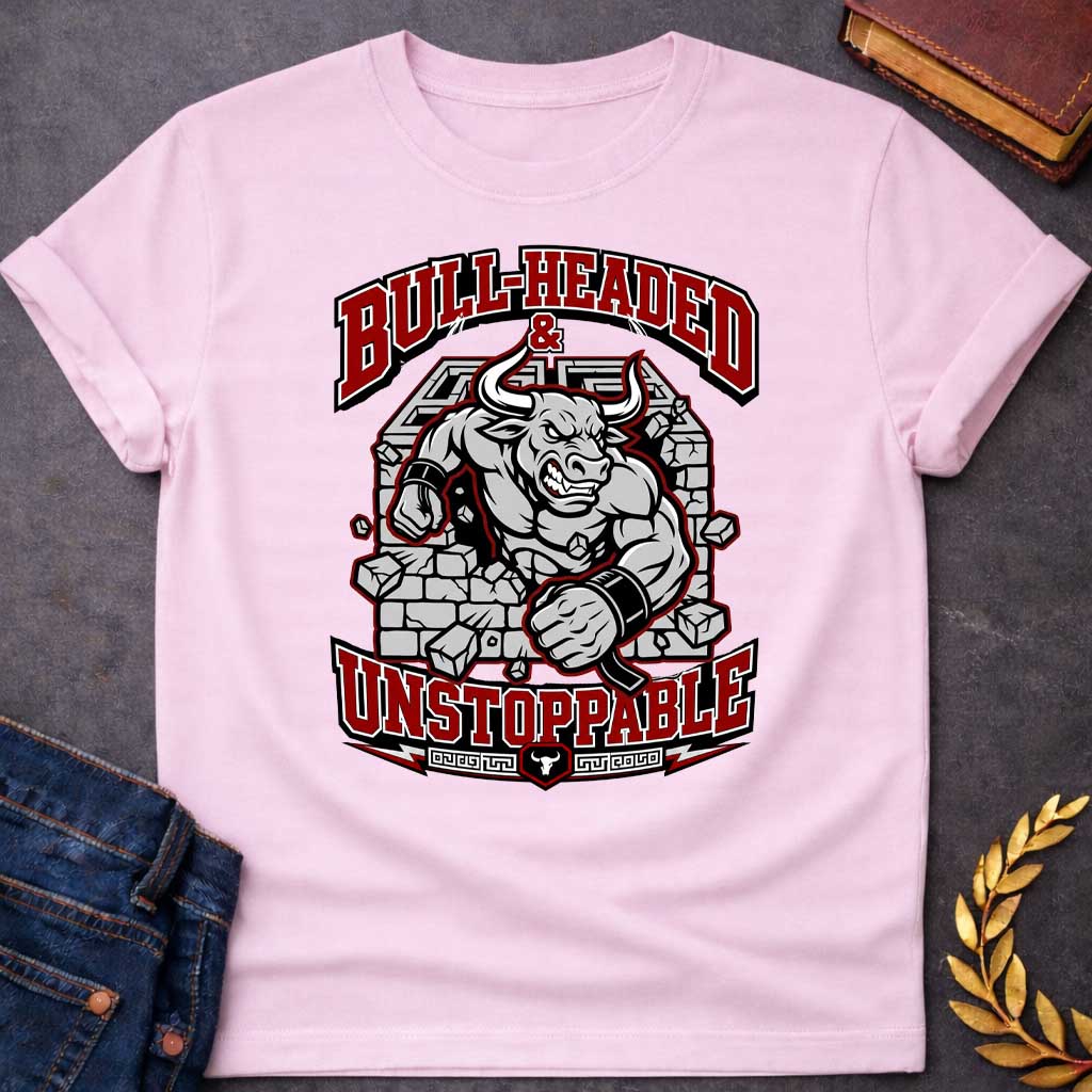 Light Pink T-shirt with a High-impact sports design featuring a muscular Minotaur bursting through a crumbling stone wall in red, gray, and white. The aggressive bull-headed figure displays defined musculature and determination. Text reads 'Bull-Headed & Unstoppable' in bold red and black lettering. Greek key pattern and bull symbol anchor the bottom. Combines Greek mythology with modern gym and sports culture, celebrating stubborn strength and unstoppable power.