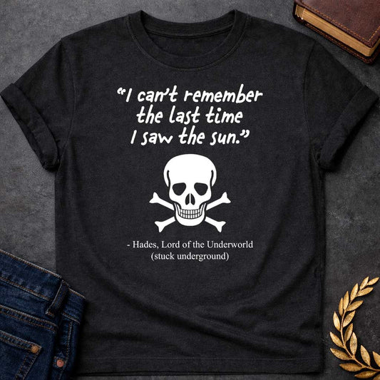 Black T-shirt graphic in black and white featuring a handwritten-style quote reading "I can't remember the last time I saw the sun." above a classic skull and crossbones illustration, with the humorous attribution below reading "- Hades, Lord of the Underworld (stuck underground)